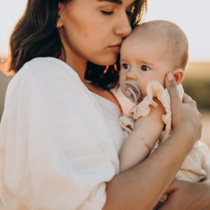 Young woman with baby daughter in carrier on the sunset